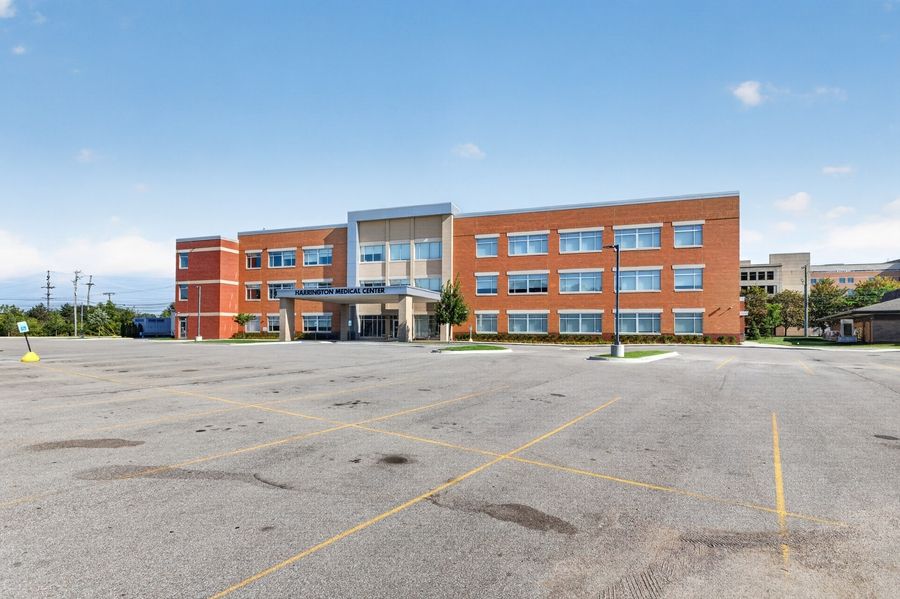 Large brick office building with blue accents and empty parking lot under partly cloudy skies.