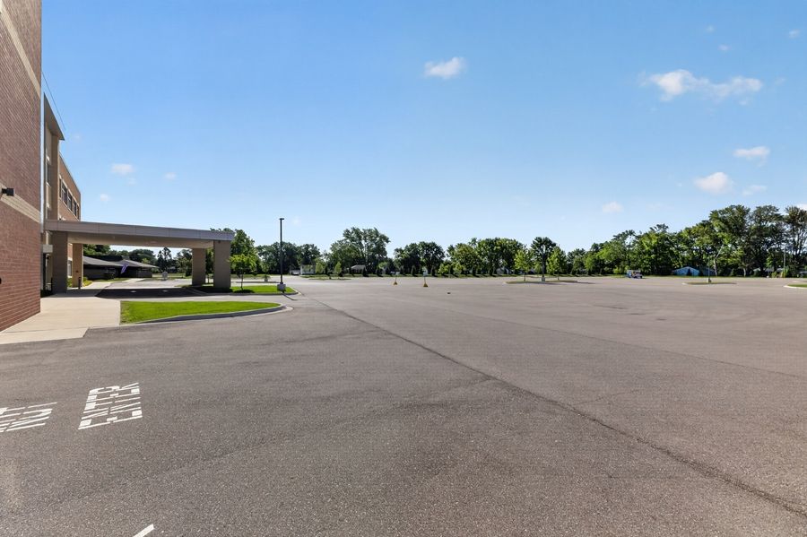 Spacious empty parking lot beside a brick building under a clear blue sky with trees in the background.