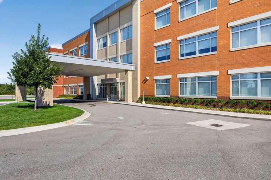 Modern brick medical office building with covered entrance, manicured landscaping, and spacious parking lot on a sunny day.