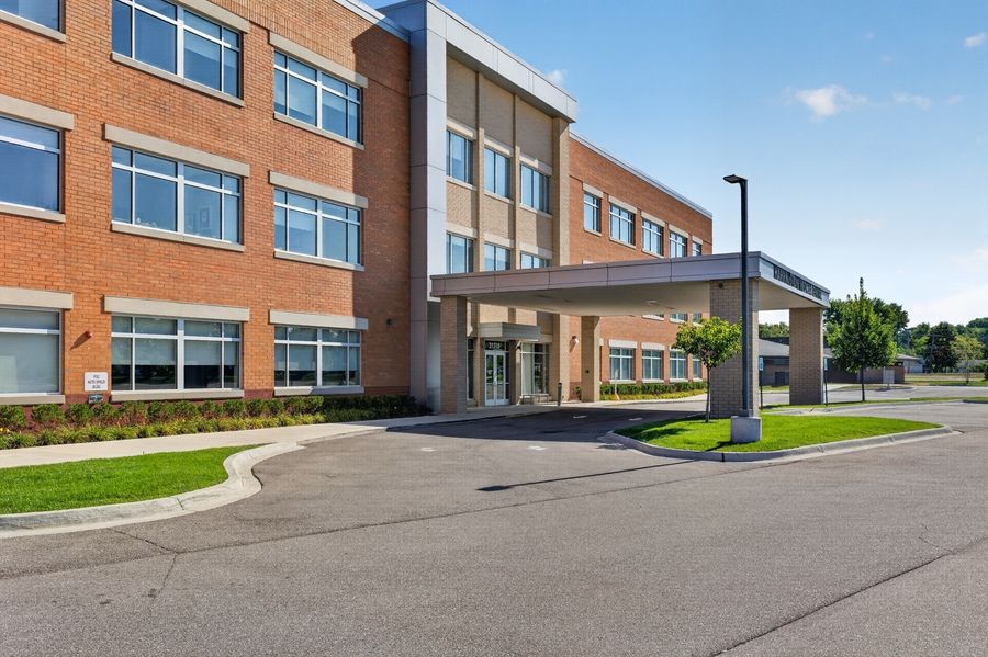 Modern brick office building with covered entrance, large windows, and manicured landscaping on a sunny day.