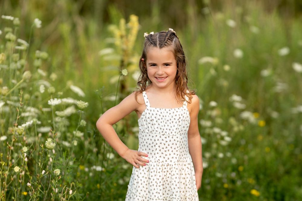 Young girl in white polka dot dress smiling in a wildflower meadow.