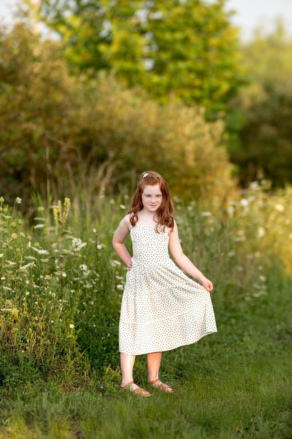 Young redhead girl in white polka dot dress posing in a wildflower meadow.