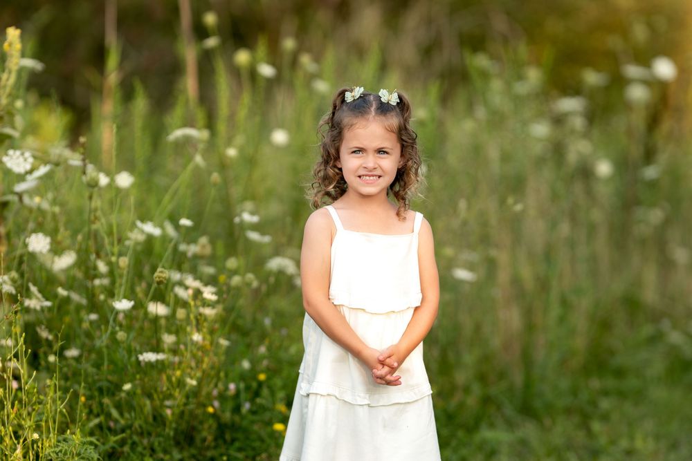 Smiling young girl with flowers in hair wearing white dress outdoors.