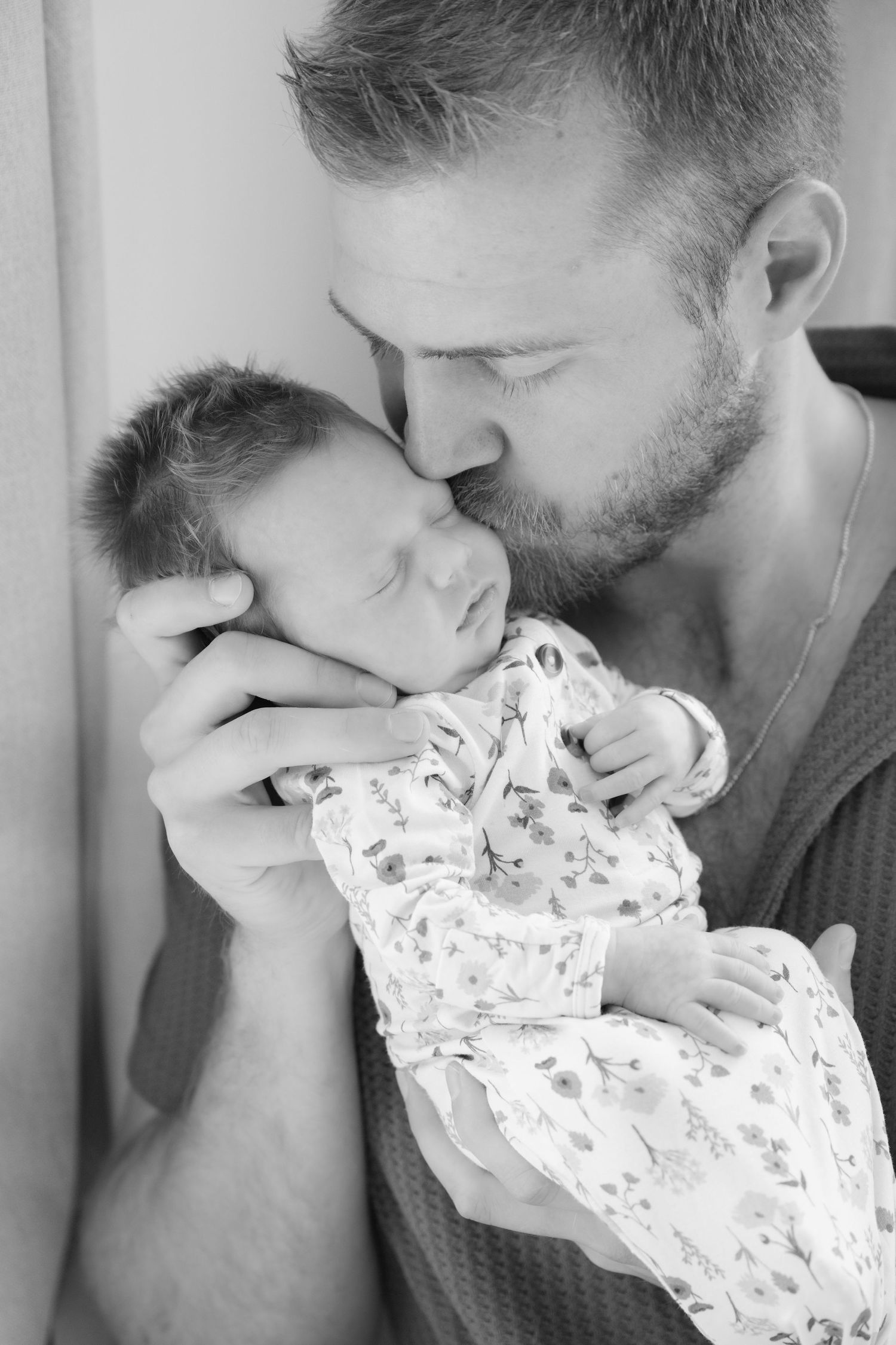 black and white image of dad kissing newborn baby's cheek during in-home lifestyle newborn session in the Twin Cities, MN.