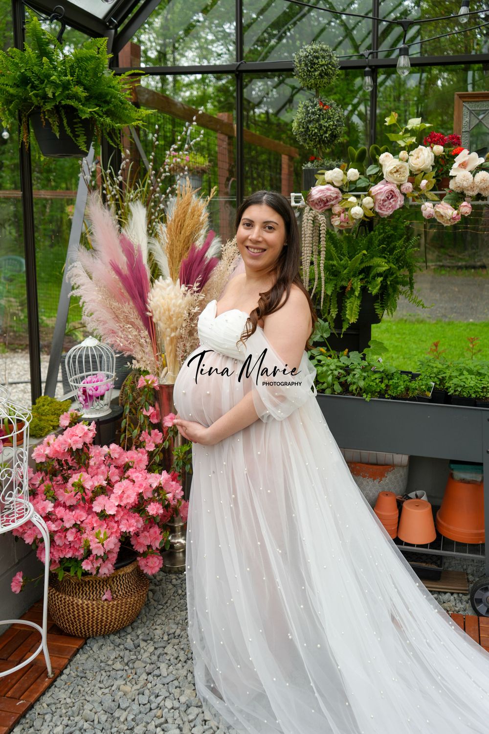 Greenhouse maternity photo featuring white flowing gown and decorative dried pampas grass.