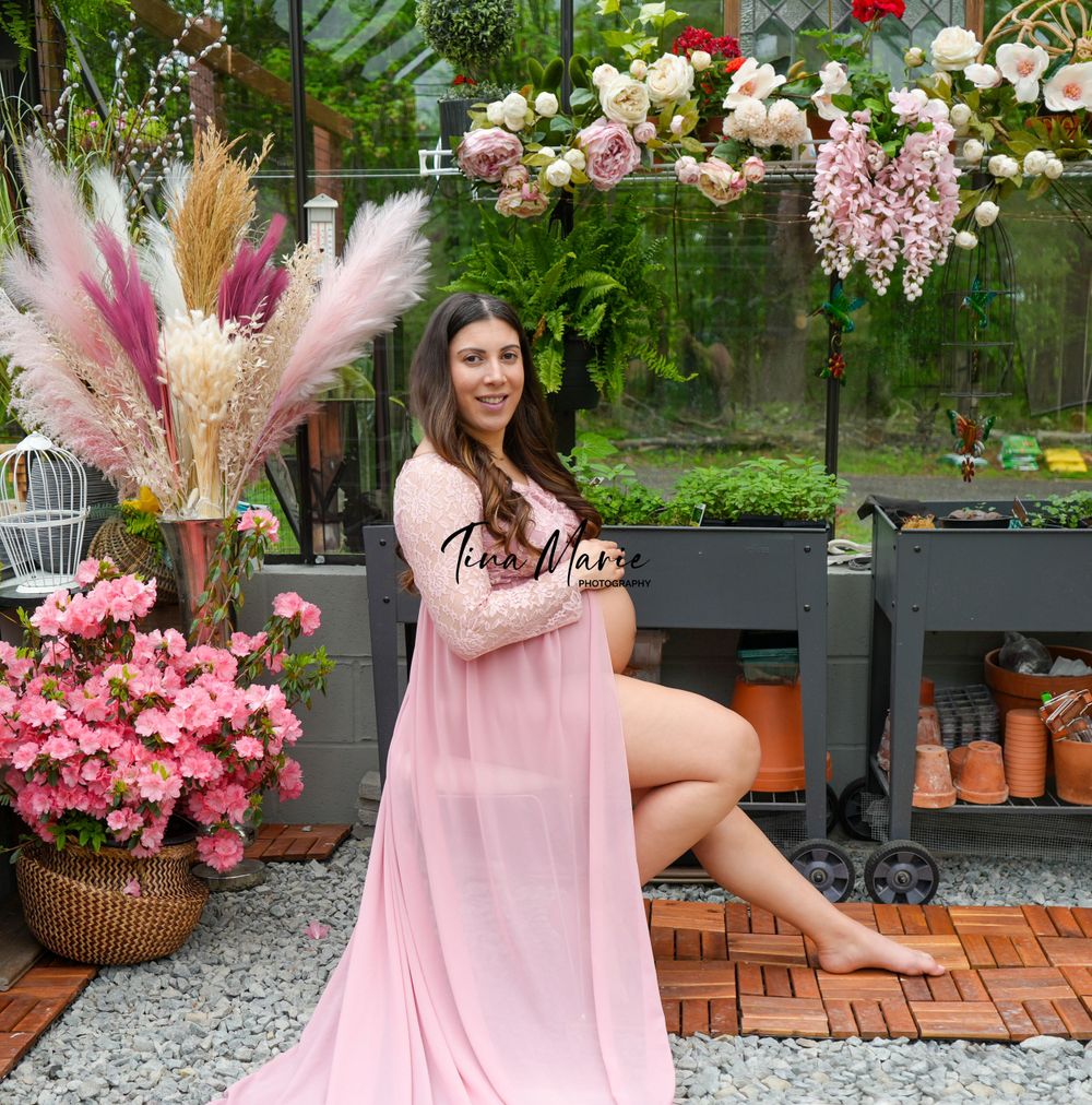 Beautiful maternity session in a greenhouse with pink florals and rustic pottery displays.