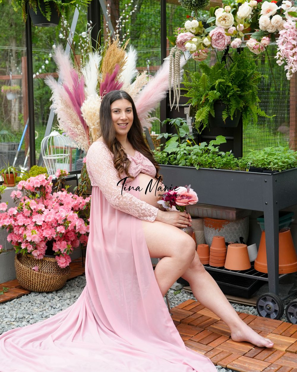 Dreamy greenhouse maternity photo featuring pink pampas grass and floral arrangements.