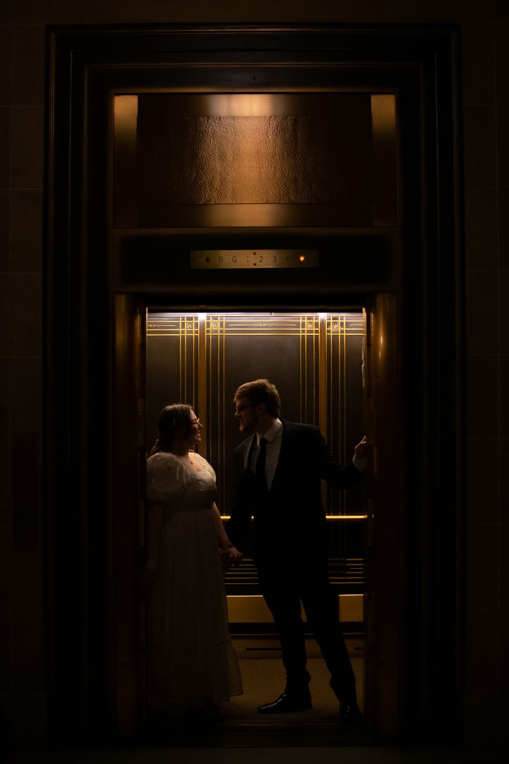 A bride and groom share an intimate moment standing together inside a dimly lit vintage elevator.