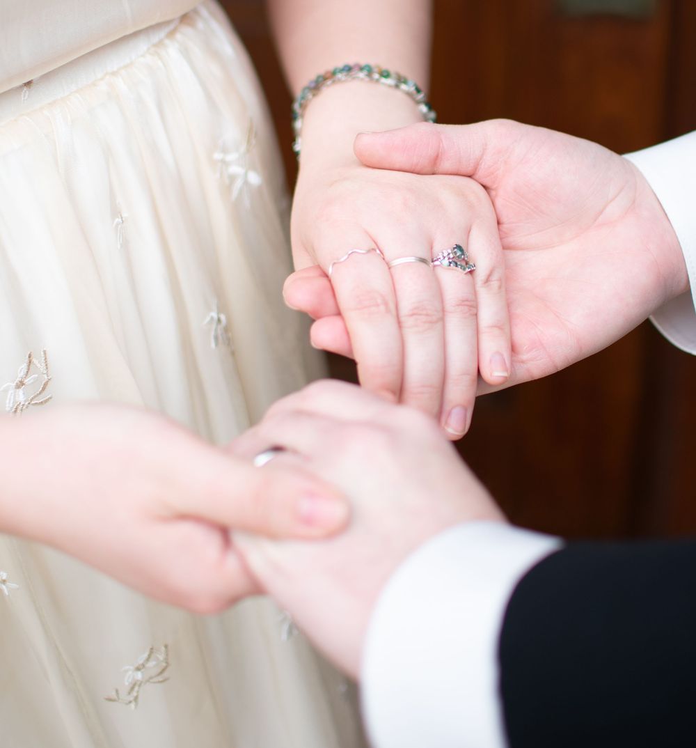 Close-up of a bride and groom holding hands showing wedding rings and a delicate bracelet.