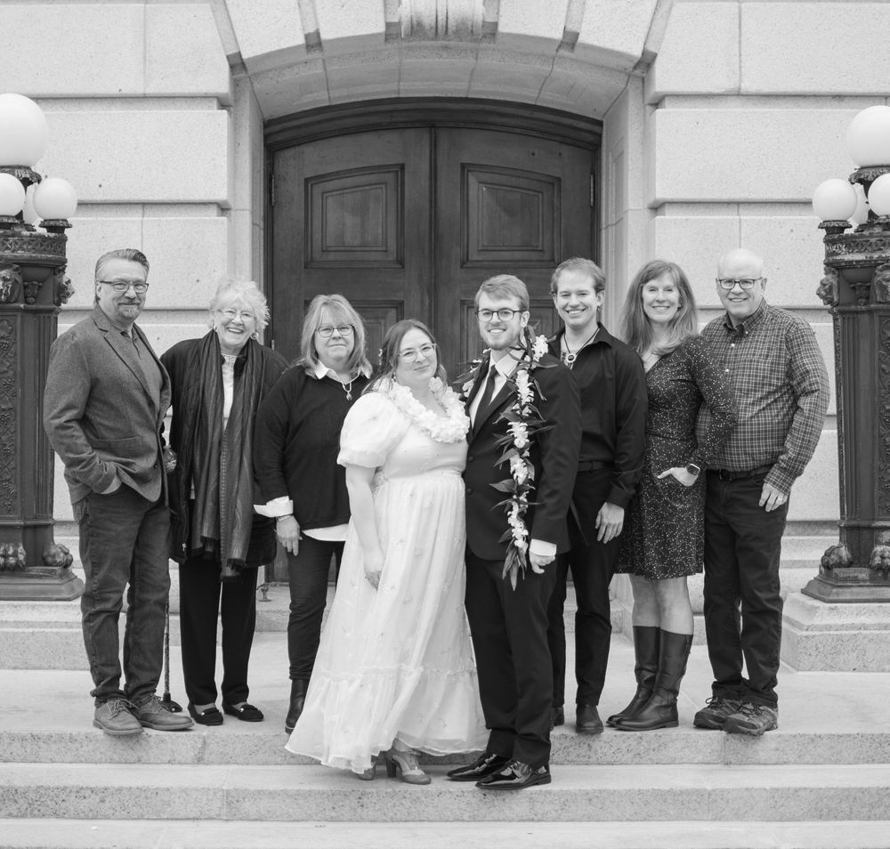 Black and white wedding portrait of couple with family on building steps after ceremony.