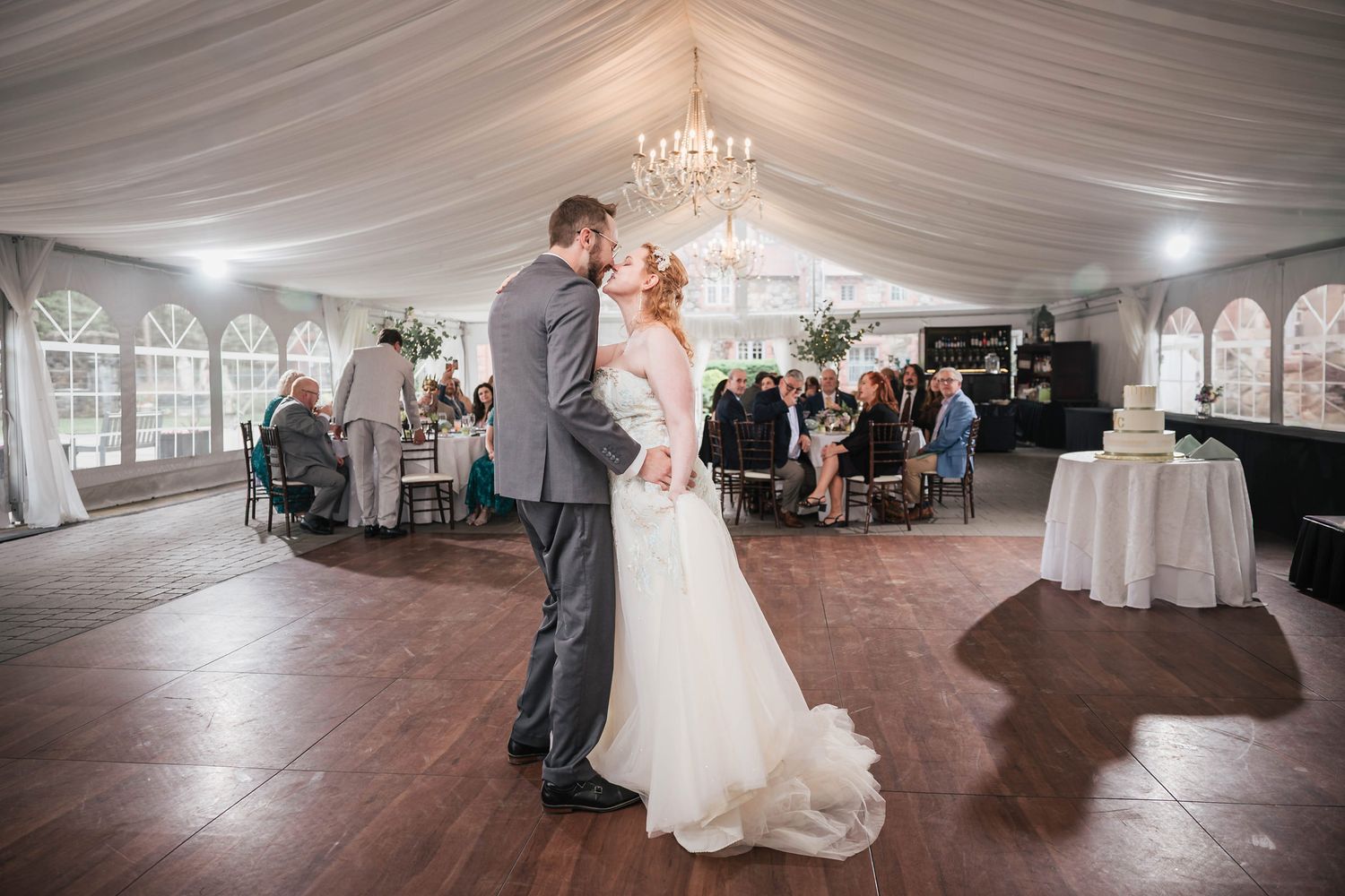 Bride and groom touching noses during their first dance, guests and the reception tent visible around them