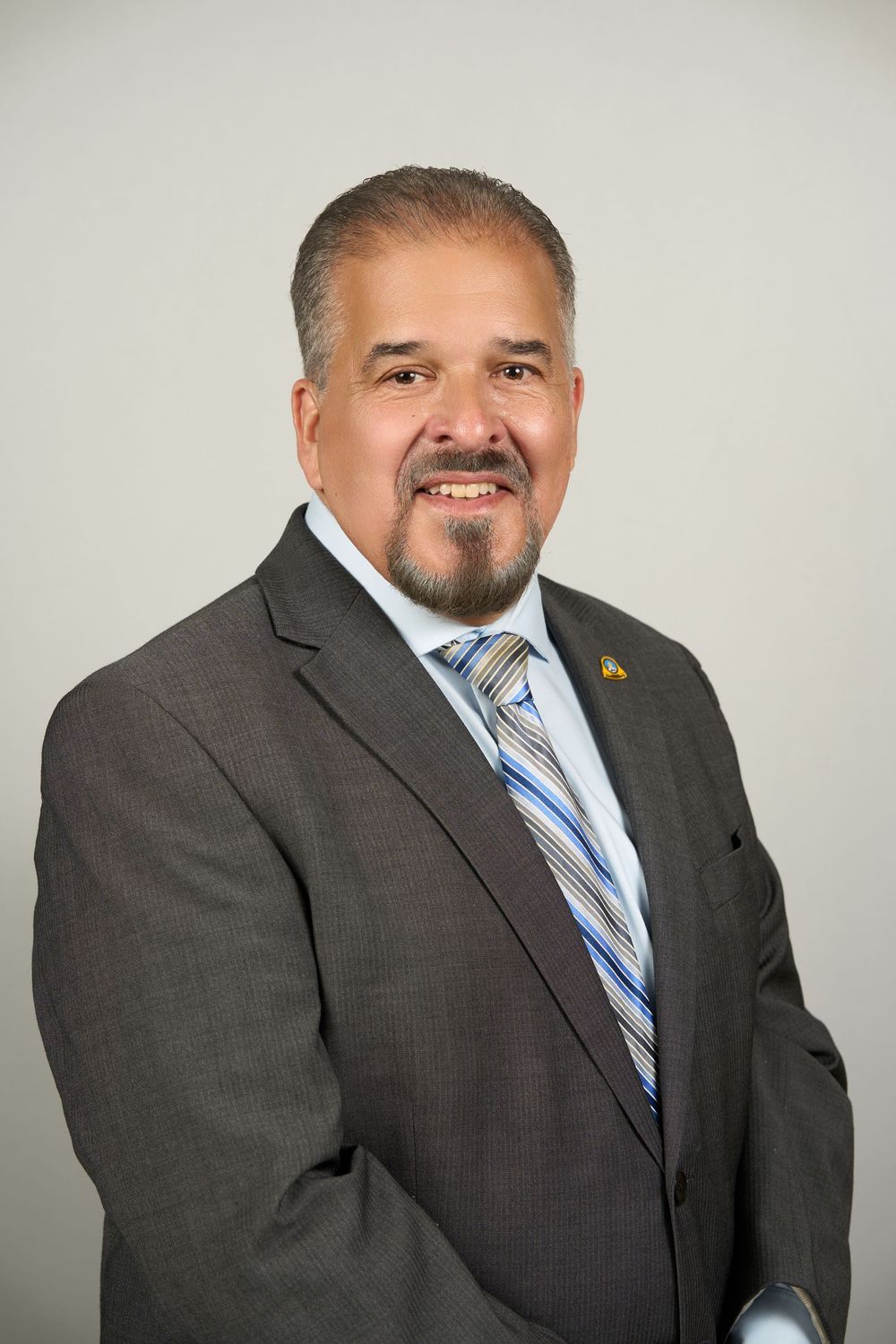Professional headshot of a smiling man in a gray suit and striped tie against a neutral background.