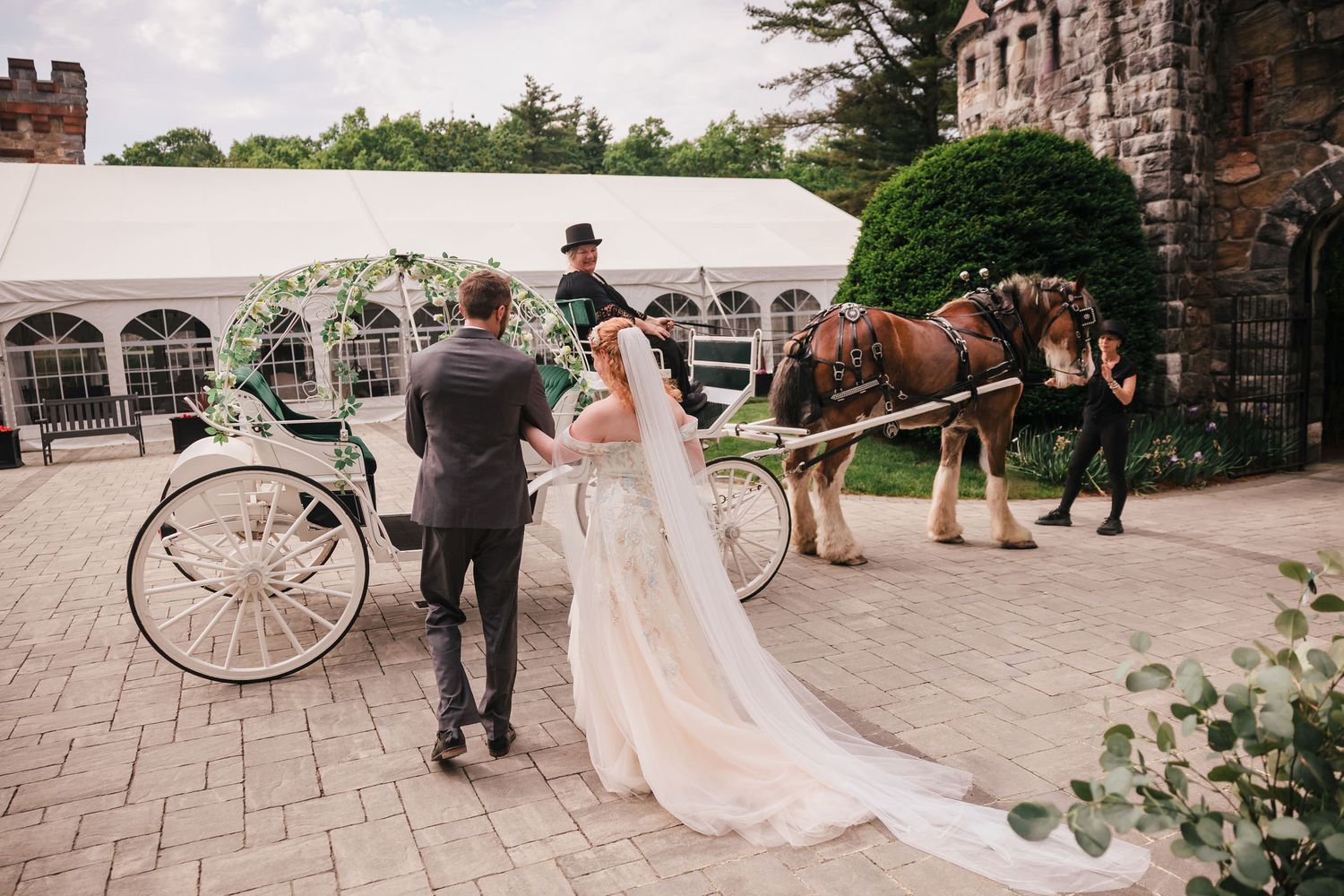 Groom helping his bride into a white horse-drawn carriage at Searles Castle in Windham, New Hampshire, after their ceremony.