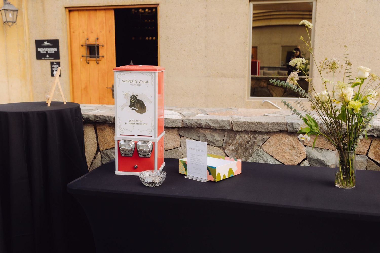 Elegant event welcome table with floral arrangement and display materials on black tablecloth.