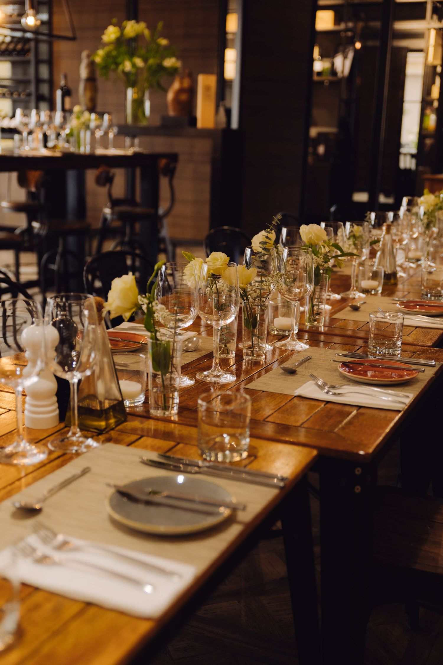 Long wooden dining table elegantly set with glassware and white floral centerpieces in restaurant.