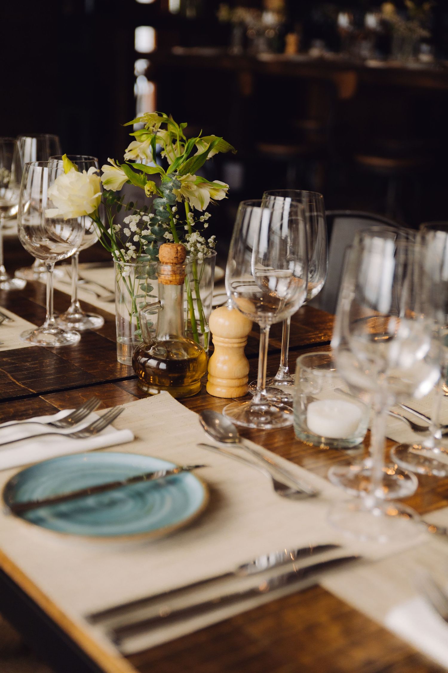 Close-up of rustic wooden dining table set with blue plates, glassware, and white flowers.