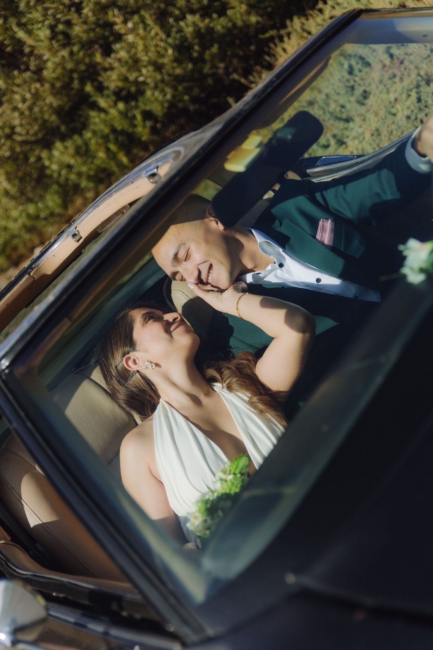 Bride and groom share an intimate moment together inside a classic convertible car on their wedding day.