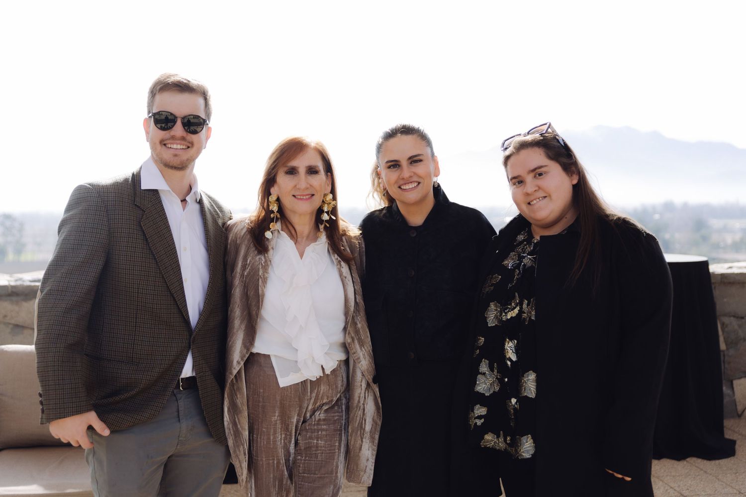 Four elegantly dressed guests posing together on outdoor terrace with scenic mountain backdrop.