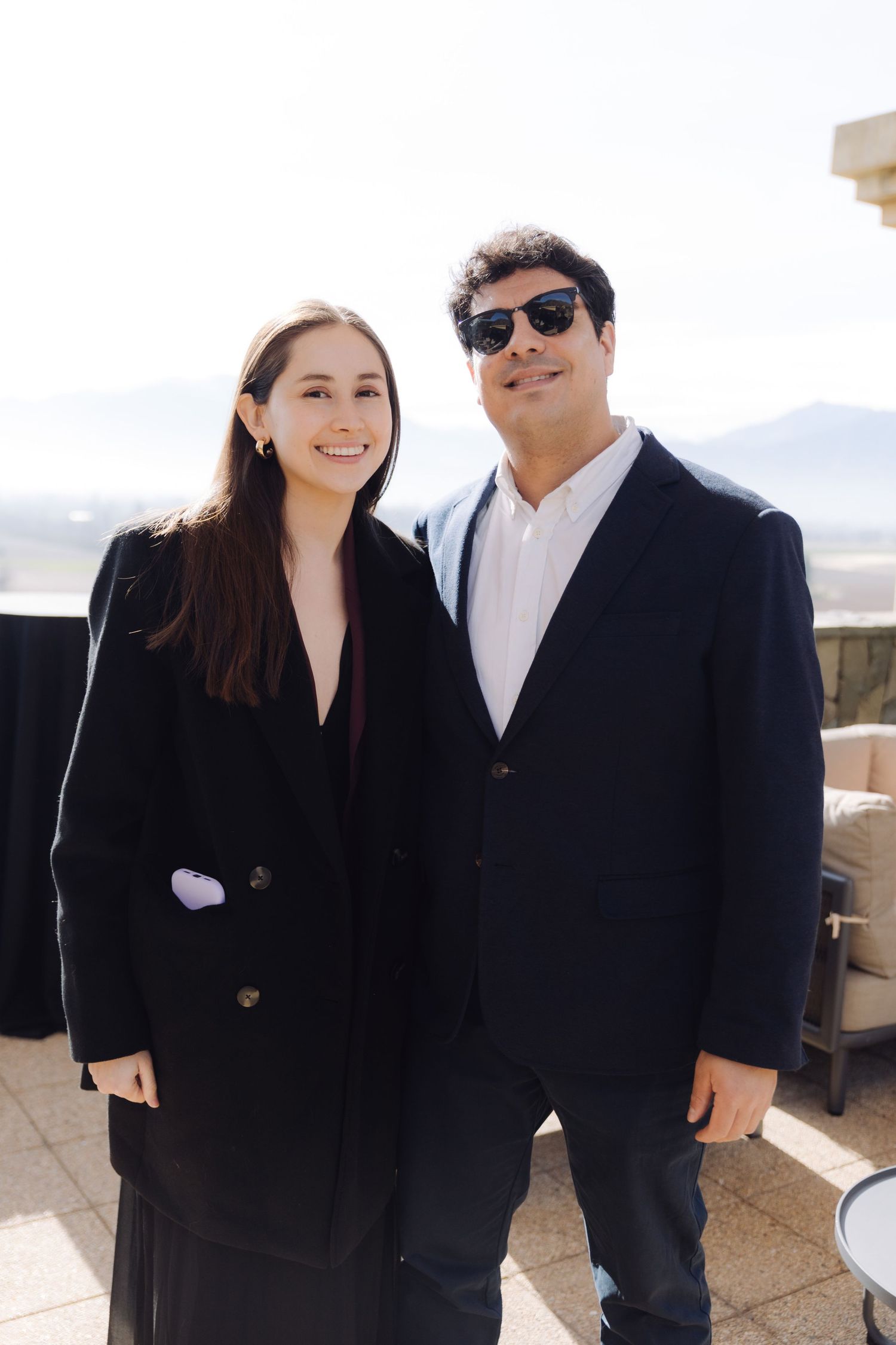 Smiling young woman and man in black suits posing together at outdoor event.