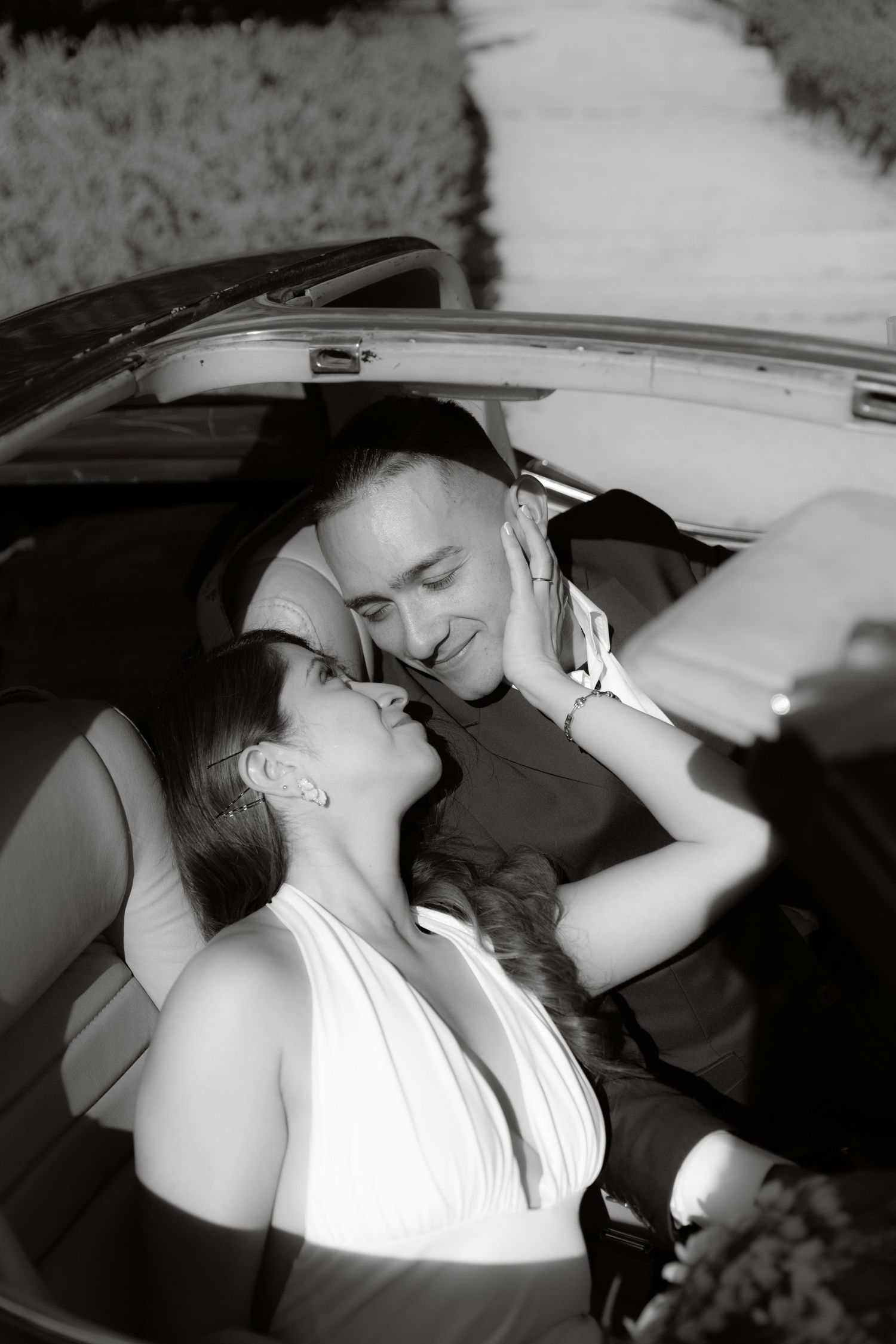 Black and white romantic photo of couple sharing intimate moment in convertible car.