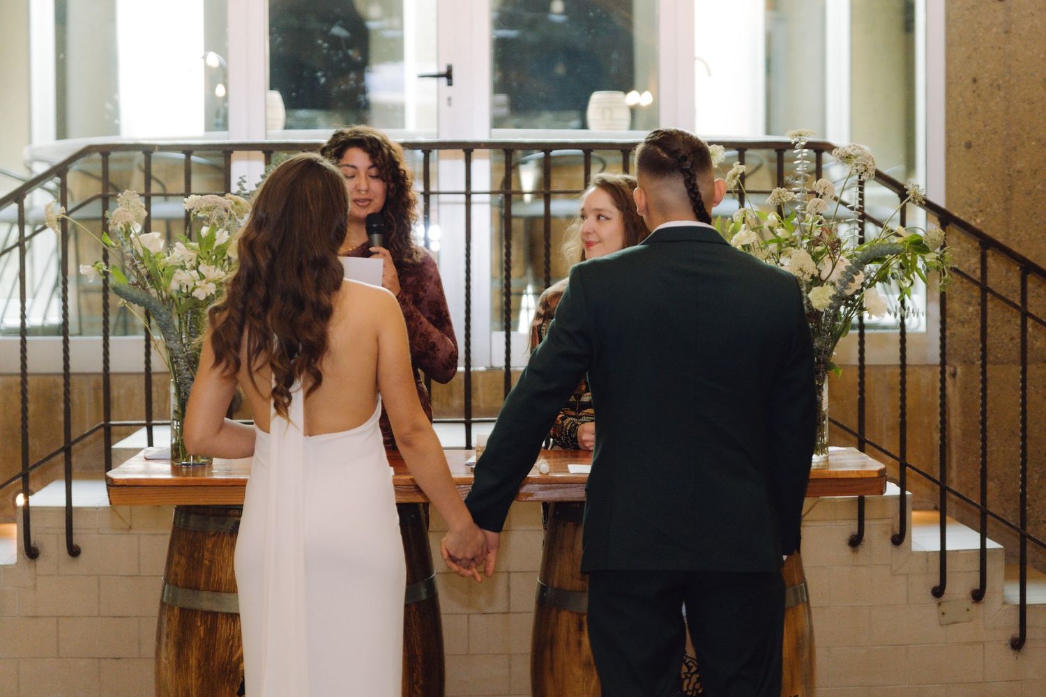 Bride and groom hold hands at altar during intimate winery wedding ceremony.