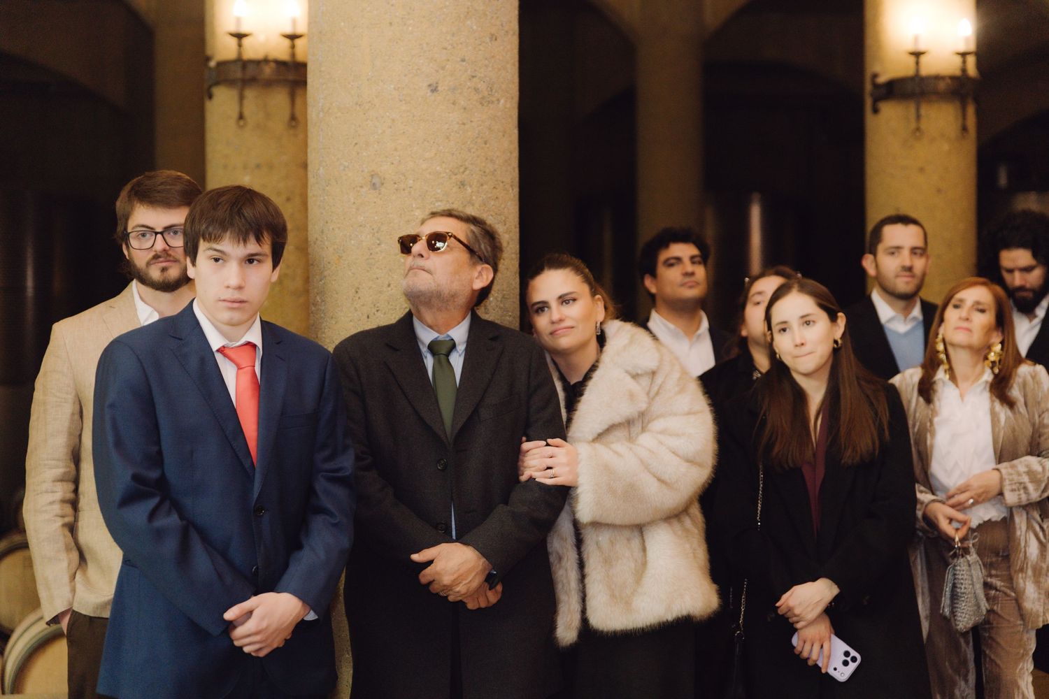 Group of elegantly dressed wedding guests gathered in ornate venue corridor.