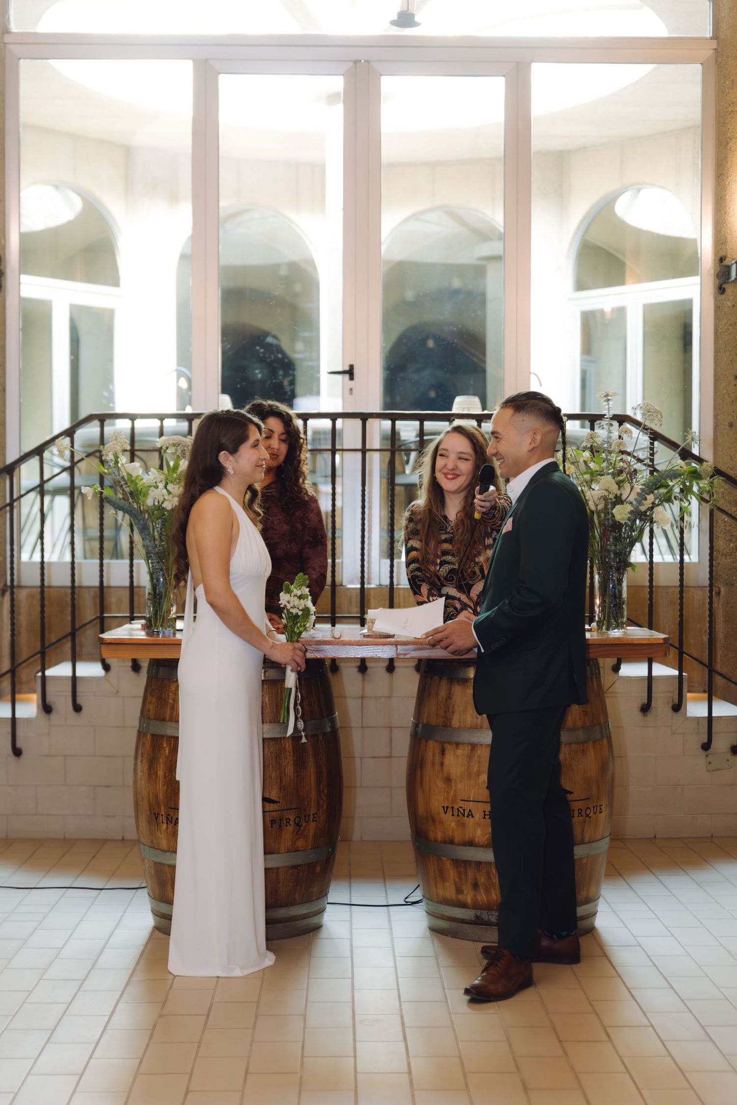 Bride and groom hold hands during intimate wedding ceremony at rustic venue with barrel altar decor.