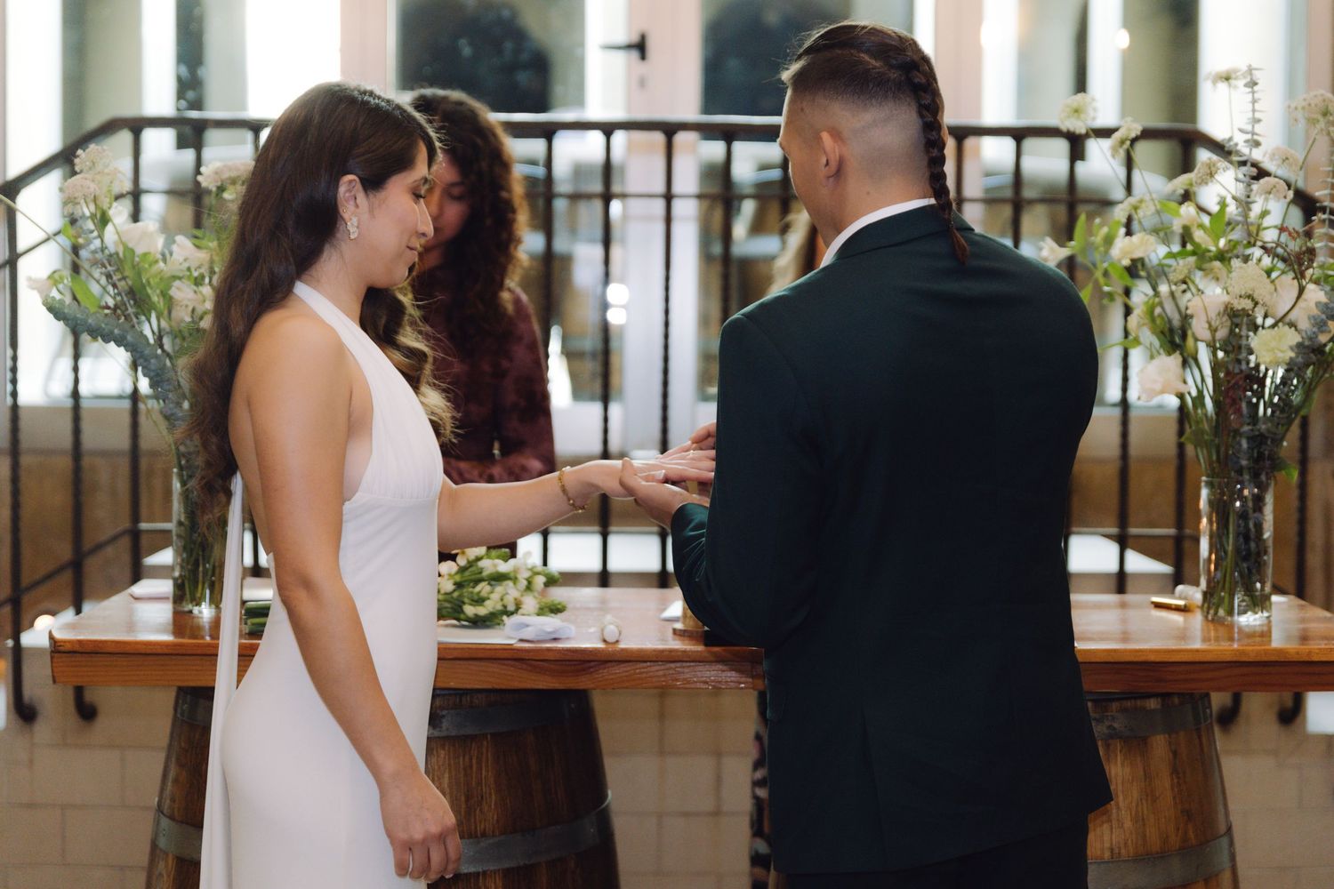 Groom places wedding ring on brides hand during emotional ceremony at rustic barrel altar venue.