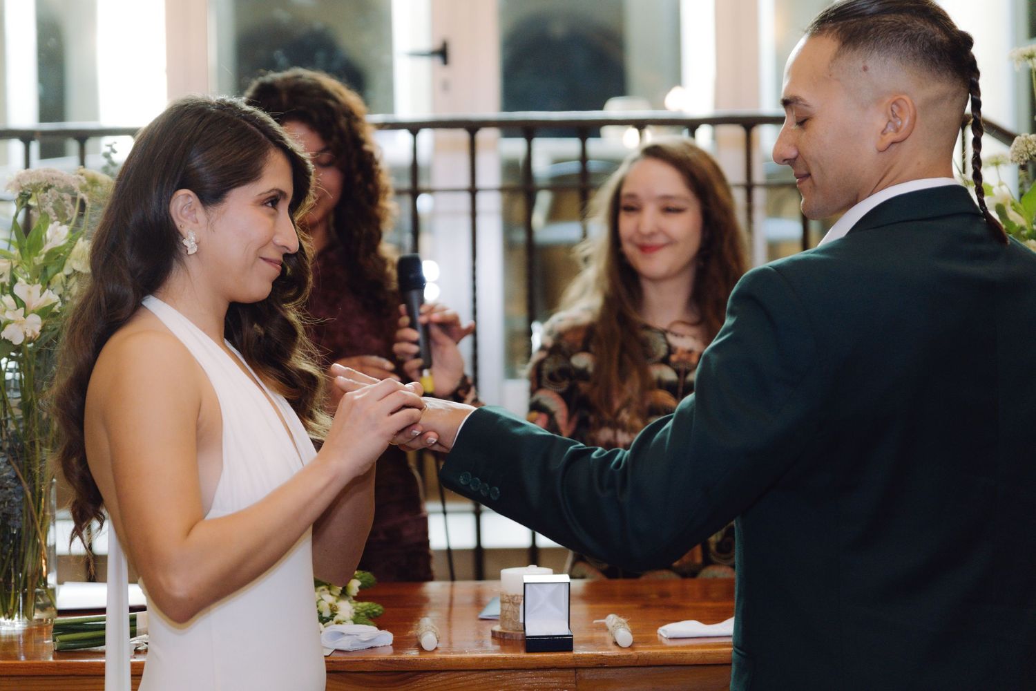 Groom slides wedding ring onto brides finger during joyful ceremony with guests watching in background.