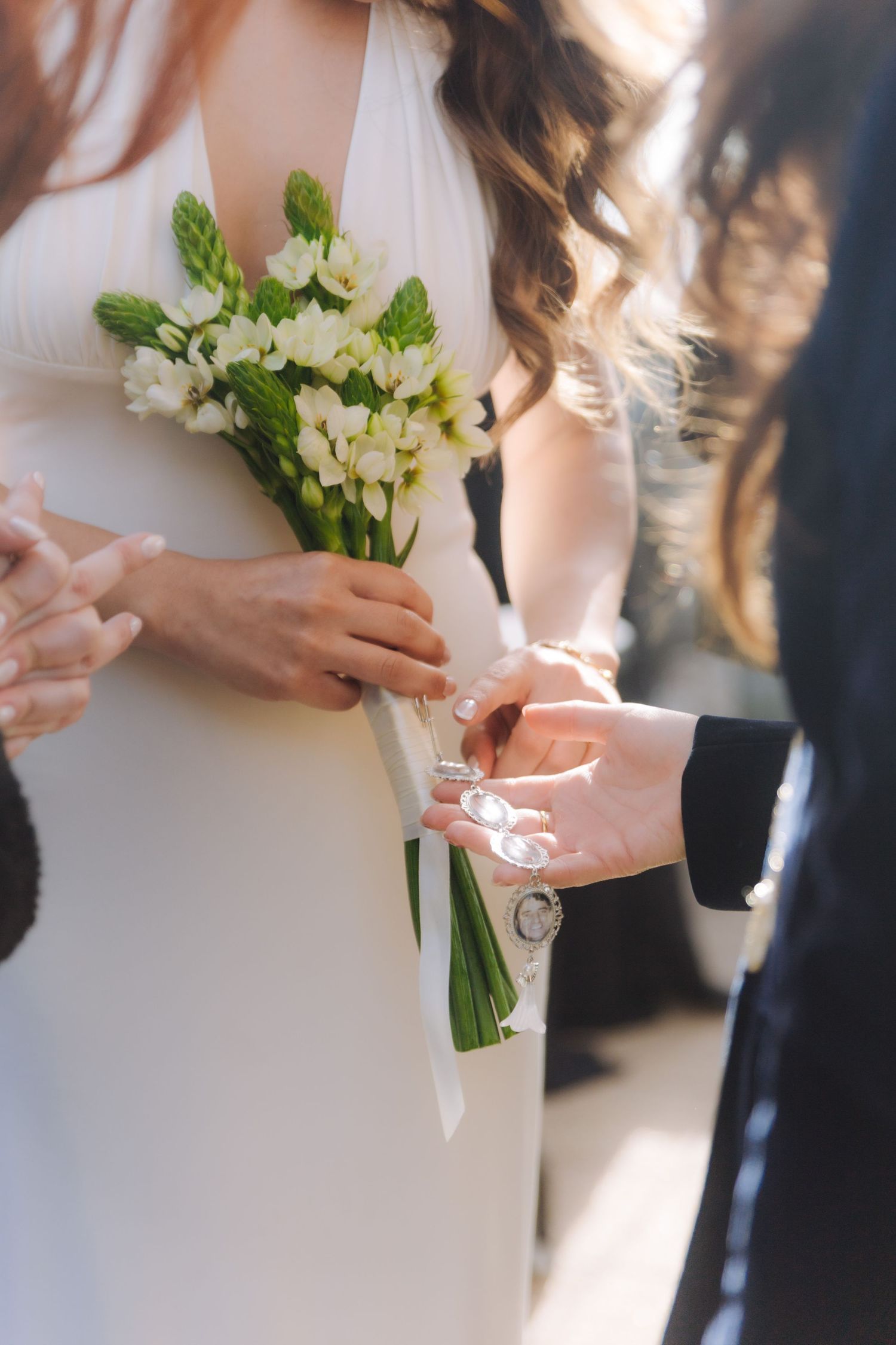 Close-up of hands attaching a decorative charm to a white wedding bouquet of fresh flowers.