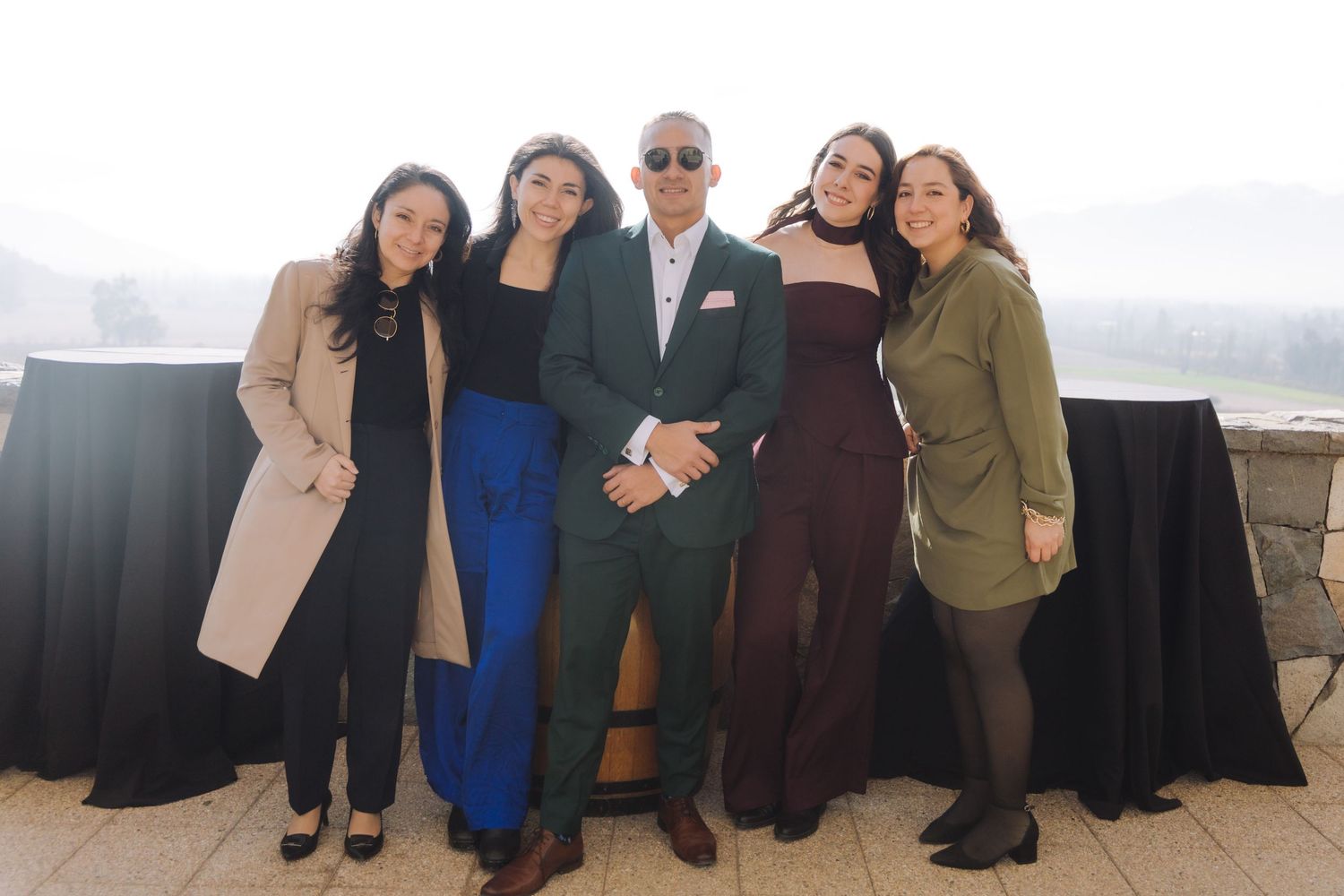 Man in green suit poses with four women on an outdoor terrace with mountain views at a wedding event.