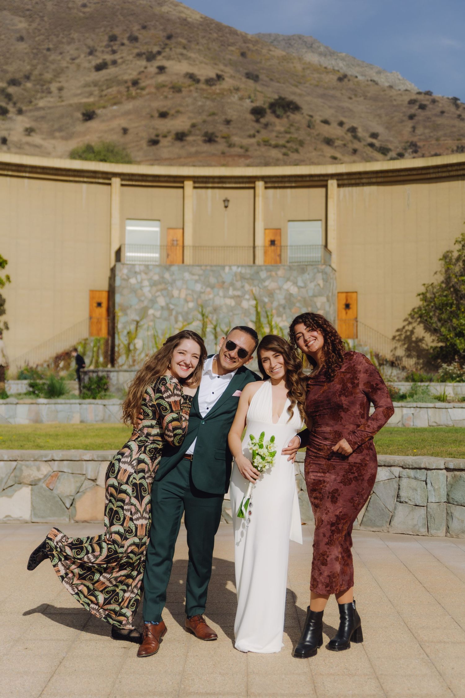 Bride and groom pose with two guests outdoors at a wedding venue with mountain backdrop.