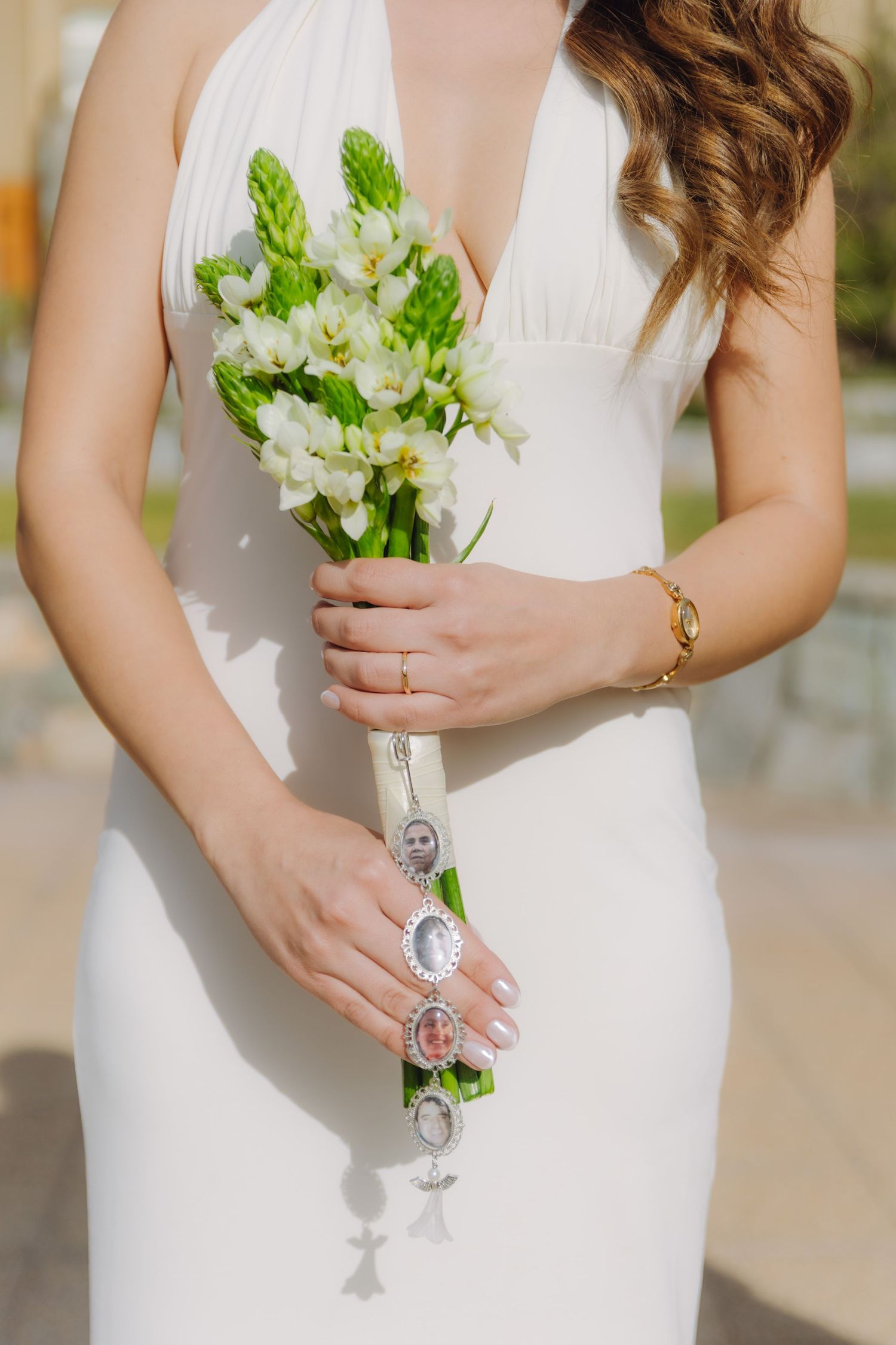 Close-up of bride in white halter gown holding a small bouquet of white flowers with charm details.