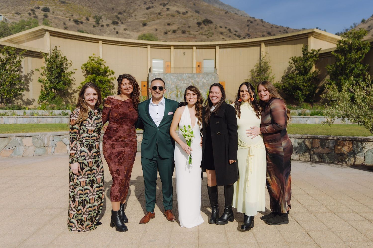 Wedding couple poses with five guests in front of a stone venue with mountain views.