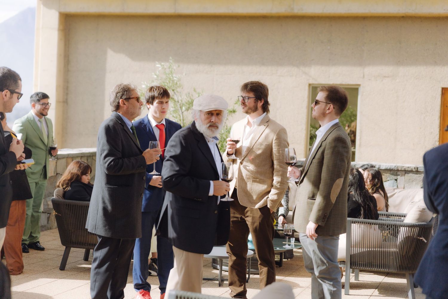 Elegantly dressed wedding guests mingle and enjoy drinks on an outdoor patio at a reception.