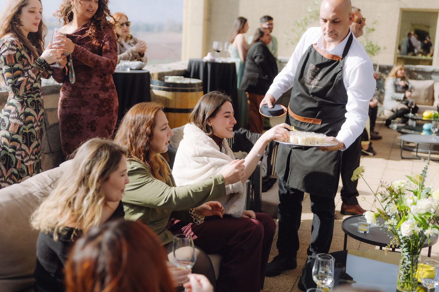 A waiter serves appetizers to seated female wedding guests at an elegant outdoor reception.