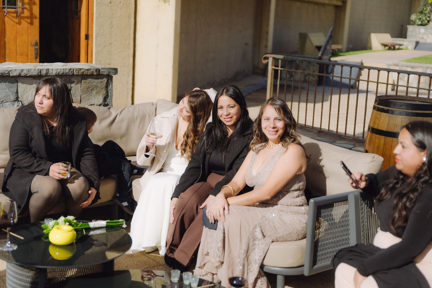 Group of female wedding guests relax and chat together on outdoor sofas at a reception.