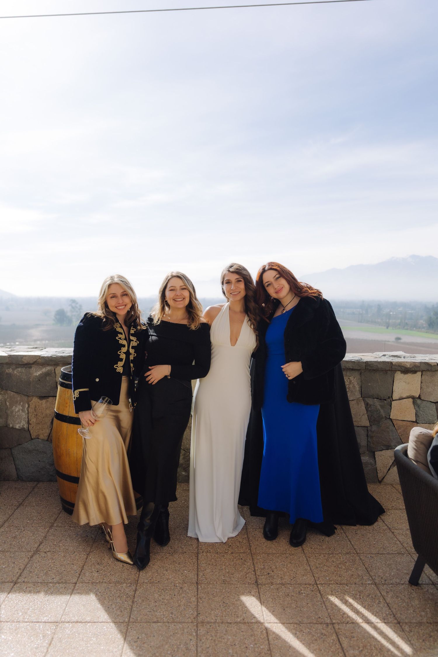 Bride in white gown poses with three guests on a stone terrace with valley views.