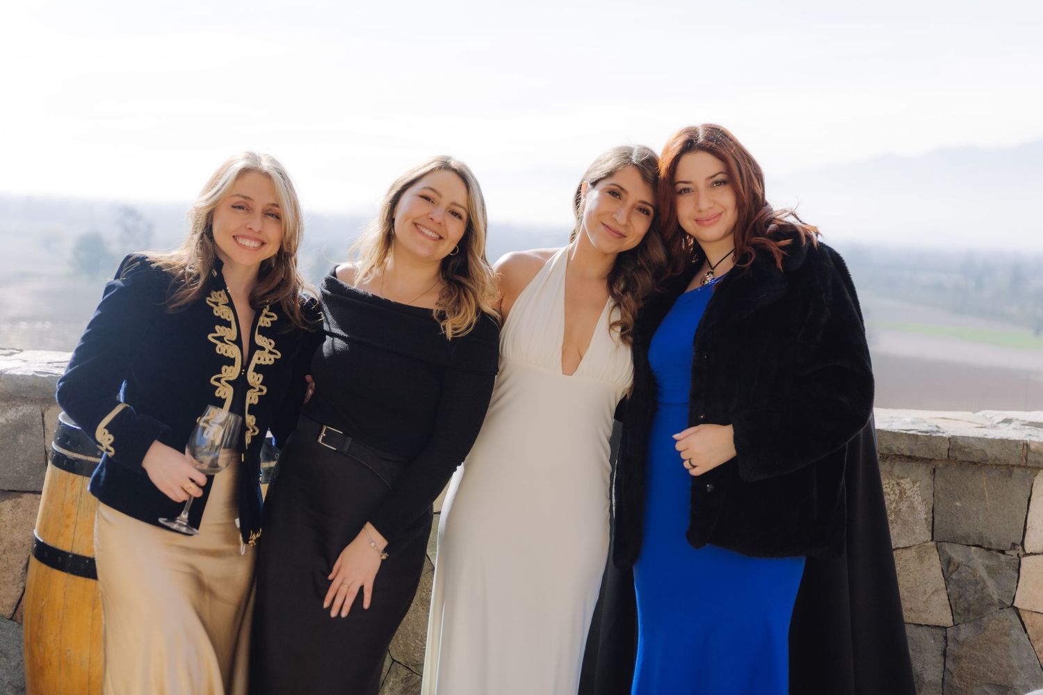 Four women pose together outdoors at a wedding, including a bride in white gown.