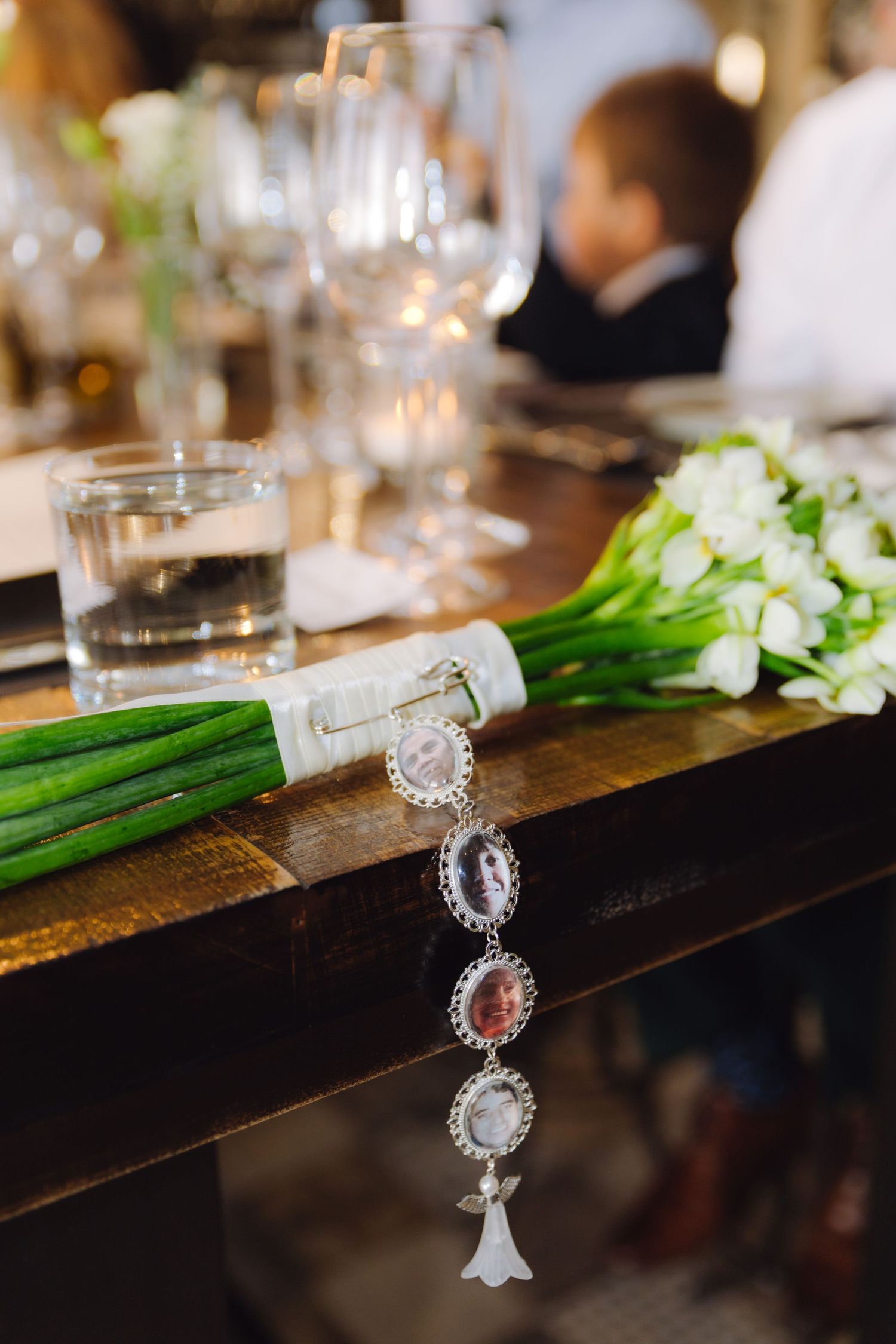 Wedding bouquet of white tulips with silver memorial photo charm on wooden table.