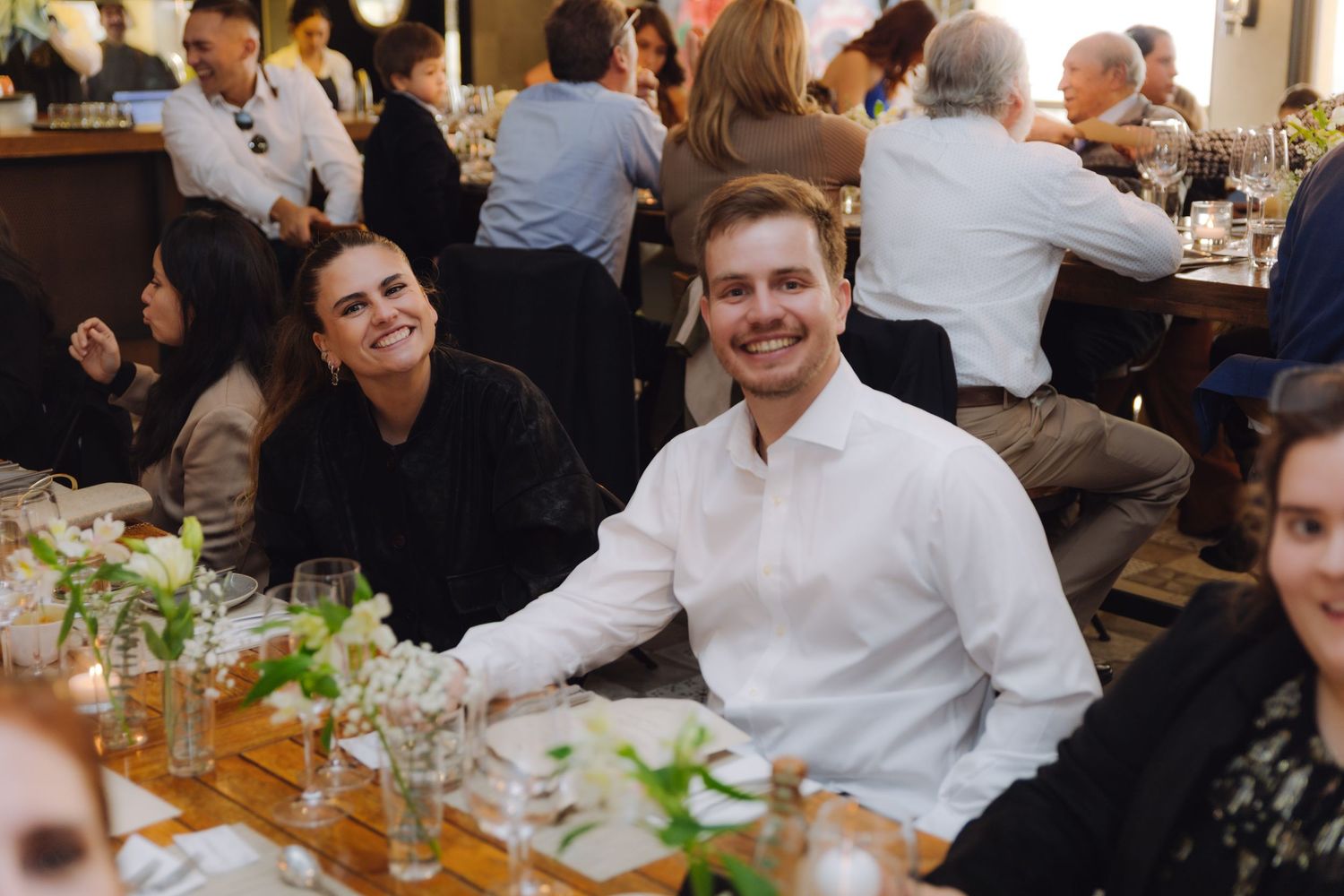 Smiling couple poses together at a wedding reception dinner table with floral decor.