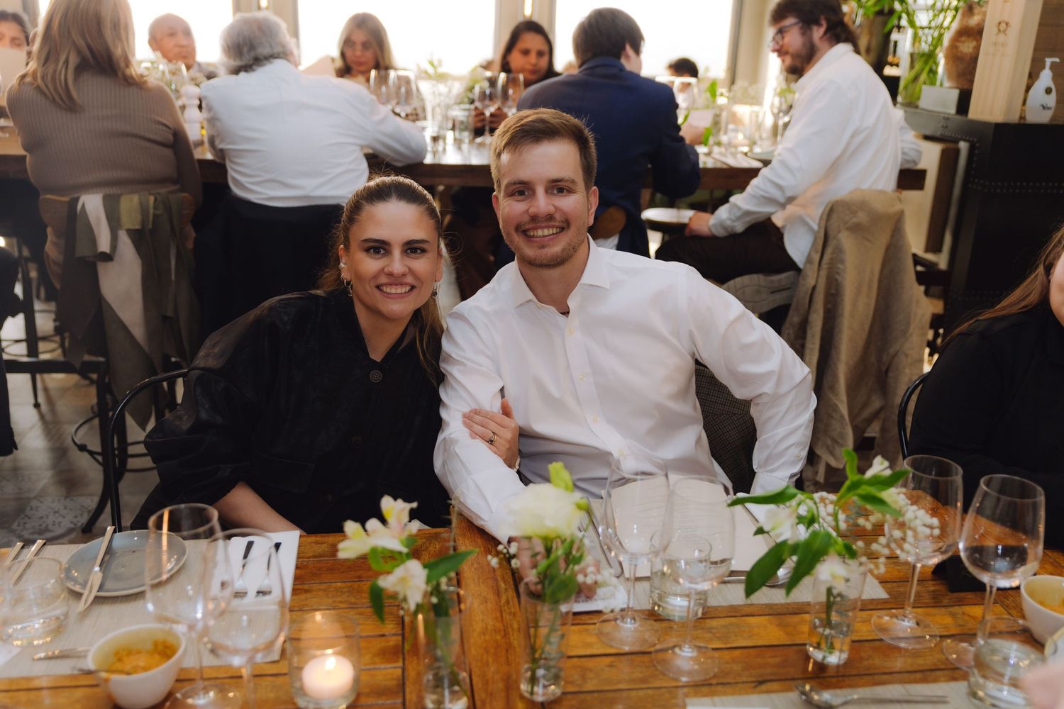 Happy couple sits arm in arm at an elegantly set wedding reception dining table.