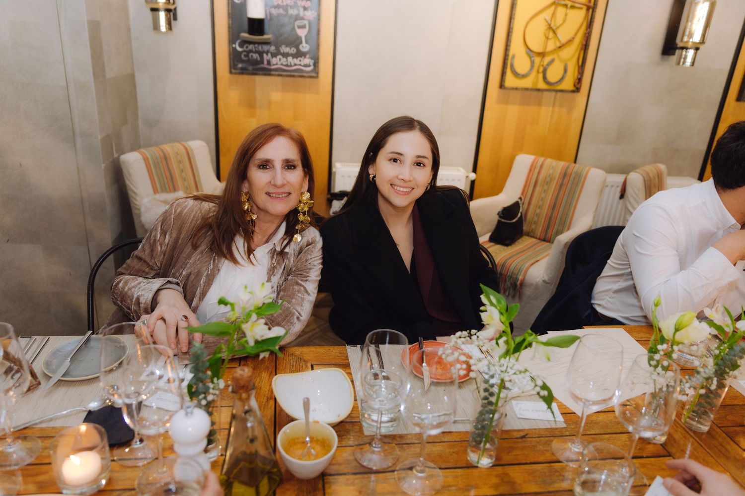 Two women smile together at a candlelit wedding reception dinner table.