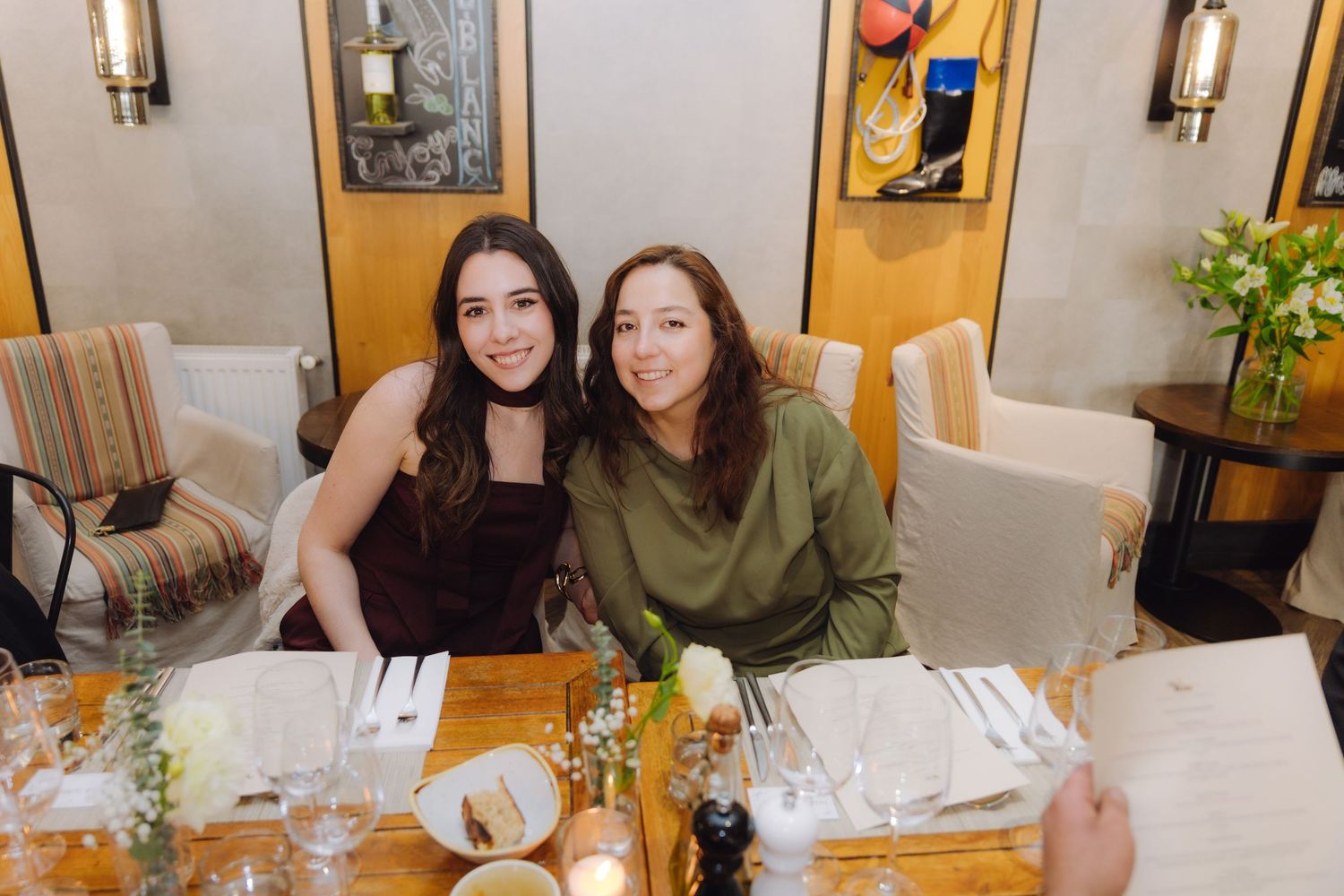 Two young women smile at the camera while seated at a wedding reception dinner table.