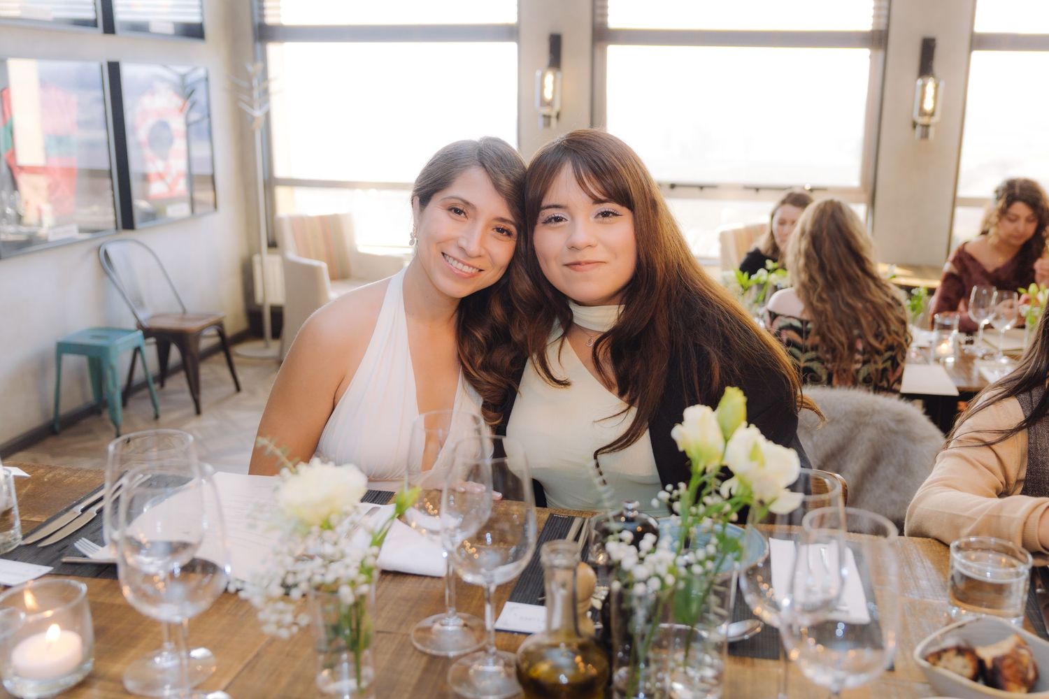 Two women pose together smiling at a beautifully set dining table with white floral centerpieces.