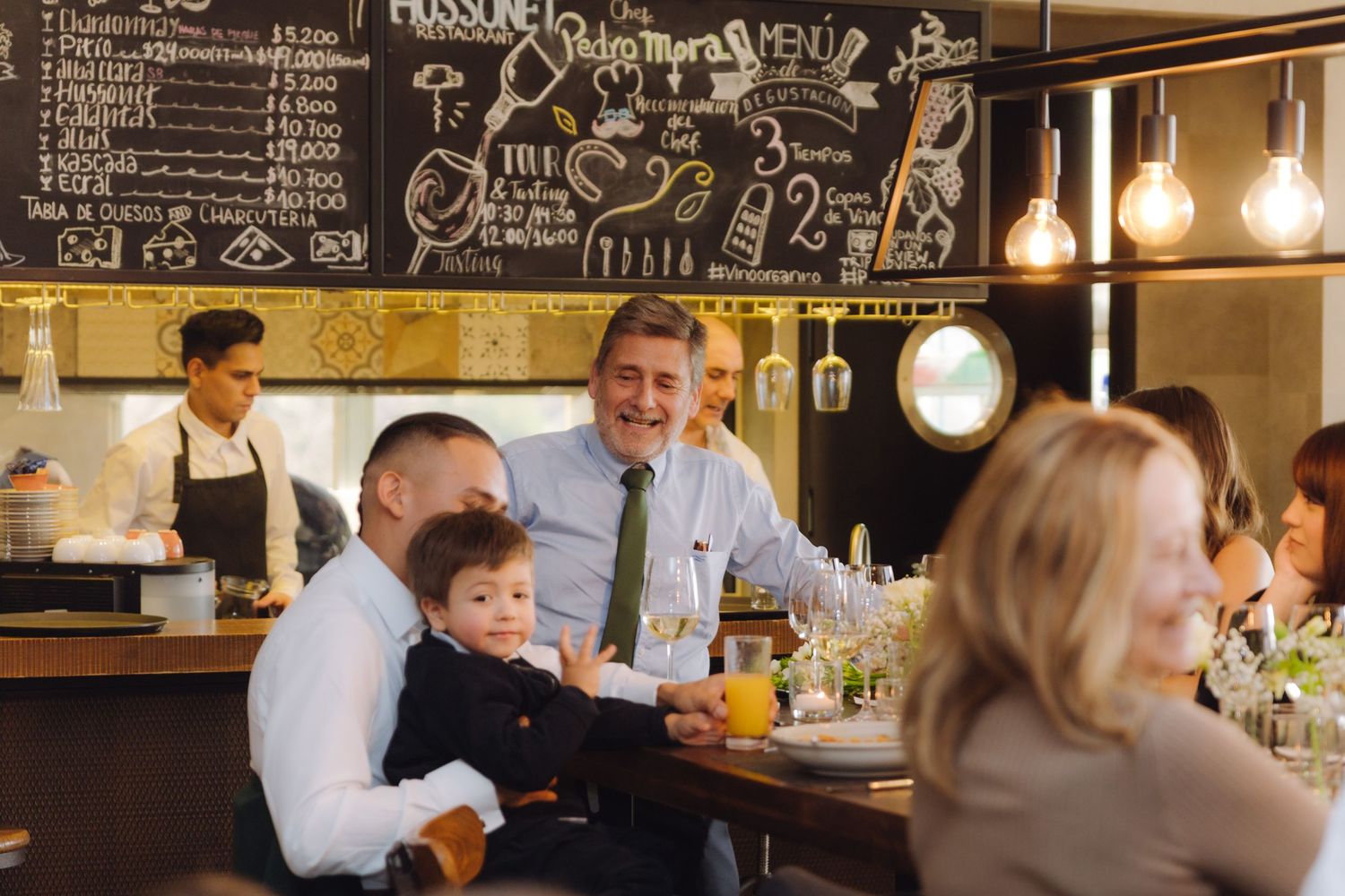 Family group with child enjoying drinks at a rustic restaurant with chalkboard menu wall.