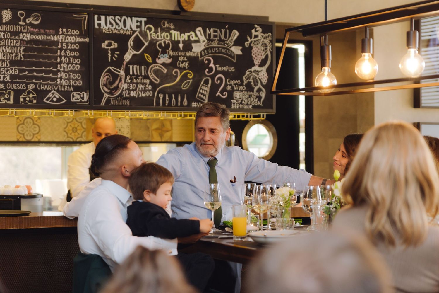 Adults and child gathered at a bar counter in a warmly lit restaurant with chalkboard menu.