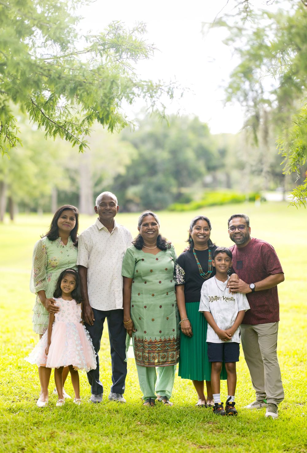Multi-generational Indian family posing together outdoors in a lush green park, smiling for a portrait photo.