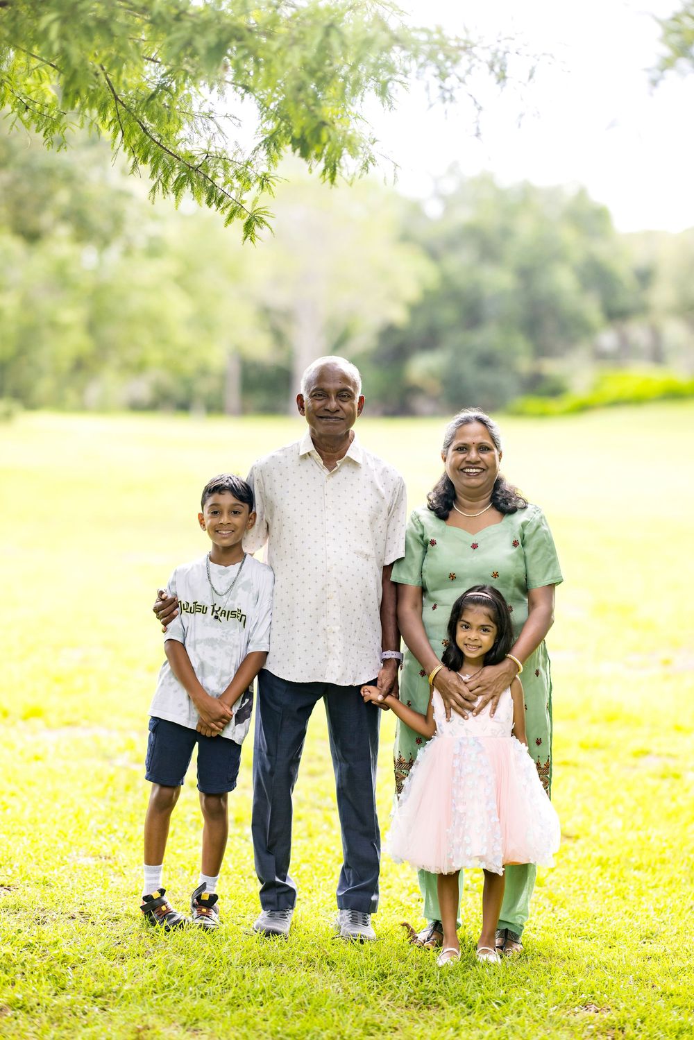 Indian grandparents posing with two young grandchildren in a lush green park, smiling together for a family portrait.