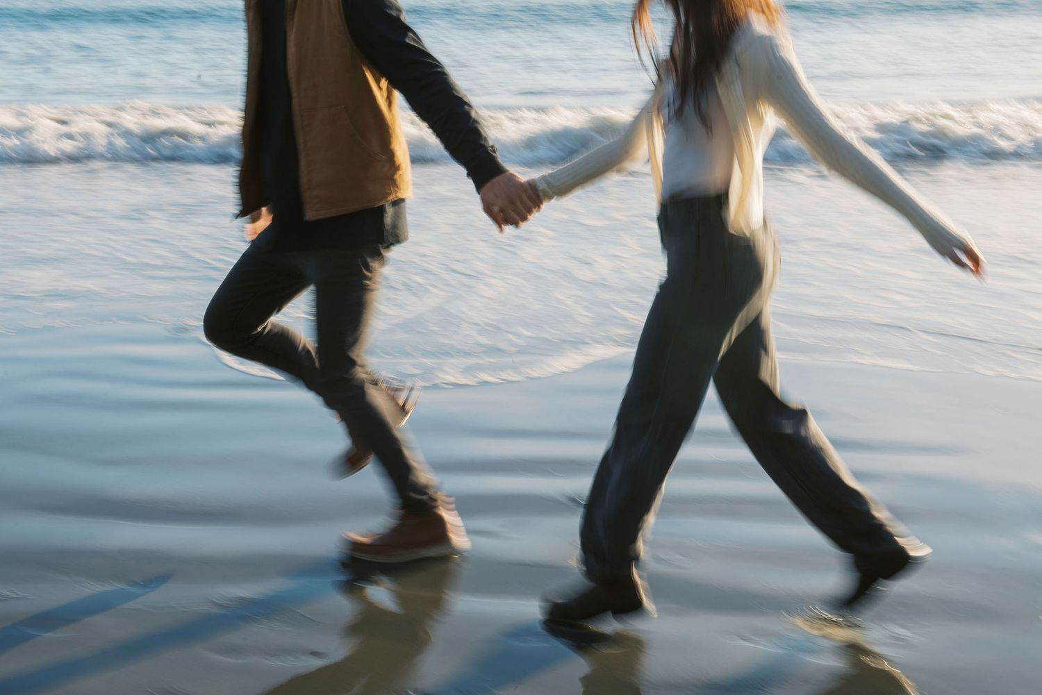 Couple walking hand in hand on rocky coastal outcrop with ocean view.
